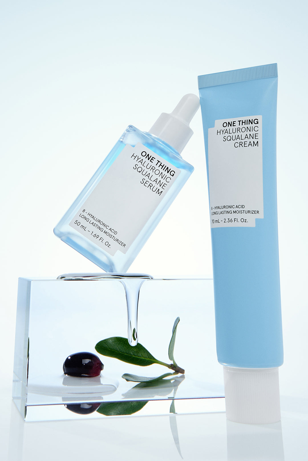 A pump bottle of Hyaluronic Squalane Cream and a small glass jar with a blue label, both displayed on a clear surface with a crystal reflecting in the background.